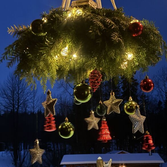 A Wreath Chandelier, lit at dusk and hung with red and green baubles and gold stars, outside at Moose Meadows Farm